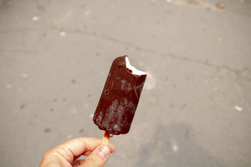 Chocolate ice cream on a stick. Ice cream is plombir in chocolate on a stick in a man's hand. First-person view. Chocolate ice-cream on a stick: cold frostbite in frost.