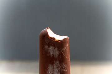 Ice cream in a hand. Ice cream - chocolate plombir. First-person view. Ice cream in chocolate on a stick: a cold frostbite in frost. Frozen sweet dessert.