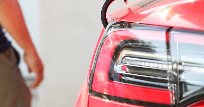 Close up of unplugging a red electric vehicle, then pulling away into a garage.