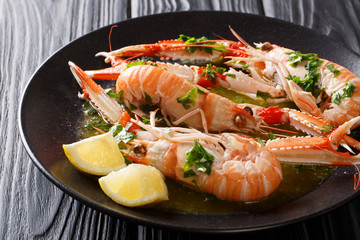 Served boiled langoustines, Dublin Bay prawn, scampi with lemon and melted butter with herbs close-up on a black table. Horizontal