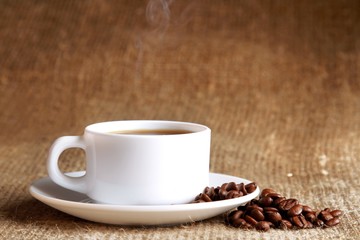 Cup of hot coffee with beans on wooden background