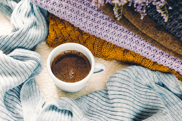 Obraz na płótnie Canvas A mug of coffee on a white blanket and a pile of knitted clothes