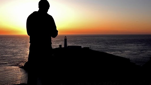 Silhouette of man making photos with smartphone during sunset at south stack lighthouse - Anglesey , Wales
