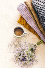Fototapeta na wymiar A mug of coffee on a white blanket and a pile of knitted clothes