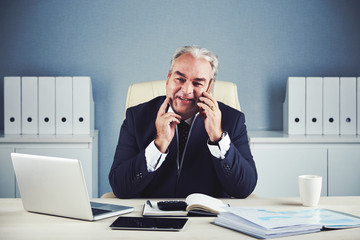 Portrait of smiling middle-aged businessman talking on phone with client