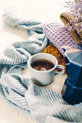 Coffee mug and blue geyser coffee pot on a white coverlet, a stack of knitted clothes and a scarf, long banner