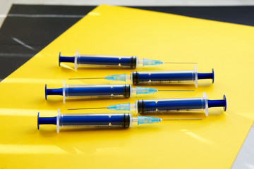 Five blue syringes on a yellow and black surface in the sun's rays.