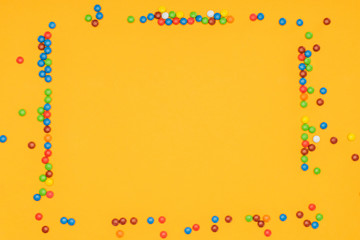 top view of delicious colored dragee candies in shape of frame isolated on orange