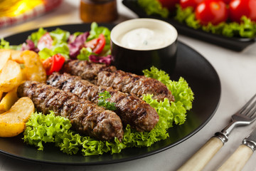 Traditional cevapcici served with baked potatoes. Stone background.