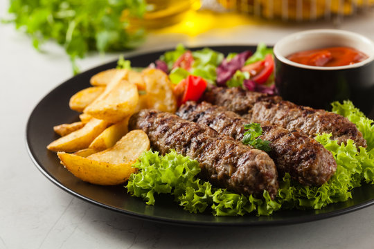 Traditional cevapcici served with baked potatoes. Stone background.