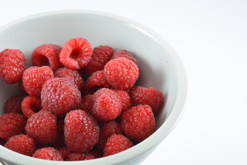 Raspberries in a white bowl on a white background