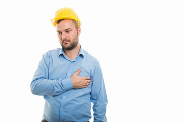 Young architect with yellow helmet showing chest pain gesture