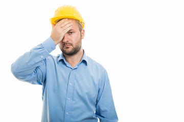 Young architect with yellow helmet showing headache gesture