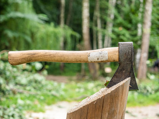 Old wooden axe used for chopping firewood embedded into wooden stump 