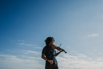 .Young musician playing the violin on a sunny summer day on the beach of Asturias in northern Spain. Expressing emotions and feelings with music. Art. Lifestyle. © lubero