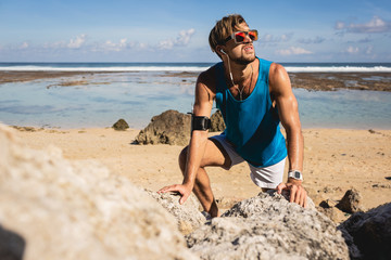sportsman looking up while climbing on rocks on beach, Bali, Indonesia