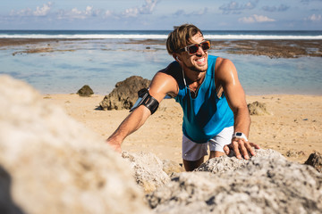 smiling sportsman climbing on rocks on beach, Bali, Indonesia