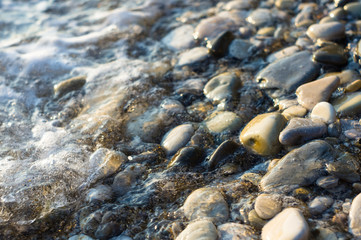 pebble stones on the sea beach, the rolling waves of the sea with foam