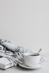 Vertical background with white cup of red tea, book and knitted blanket on wooden table, copy space. Hygge concept. Tea break