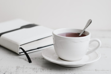 Hibiscus tea in white cup and white book on wooden table. Tea break. Reading, learning or planning during breakfast tea