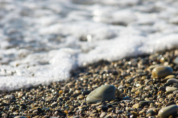 pebble stones on the sea beach, the rolling waves of the sea with foam