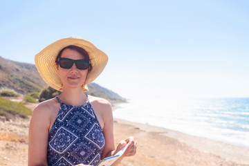 Middle-aged woman with sunglasses and a hat on the Mediterranean coast.