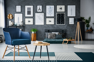 Blue armchair next to wooden table in spacious living room interior with gallery and lamp. Real photo with blurred background