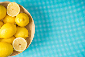 Top view of yellow lemons in wooden plate on turquoise background with copy space