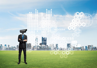 Camera headed man standing on green grass against modern cityscape