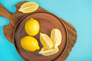 top view of yellow lemons in ceramic plate on wooden cutting board on turquoise
