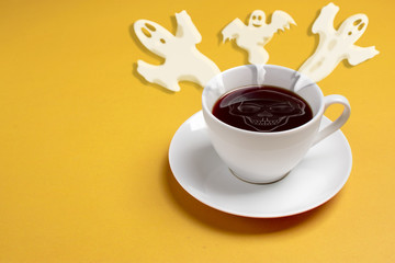 cream in the form of a ghost, witches and bats flying out of a white cup with black coffee on a yellow background Flat lay Concept Halloween party Copy space Place for text