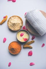 Ayurvedic face pack/mask using Gram Flour/besan, Haldi & milk ubtan placed in brass bowls with rose petals, scrub  and white napkin. selective focus