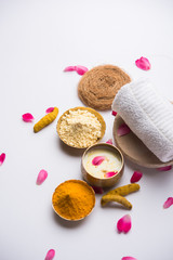 Ayurvedic face pack/mask using Gram Flour/besan, Haldi & milk ubtan placed in brass bowls with rose petals, scrub  and white napkin. selective focus