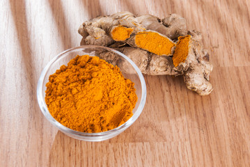 Turmeric powder and fresh turmeric on wooden background.