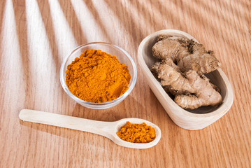 Turmeric powder and fresh turmeric on wooden background.