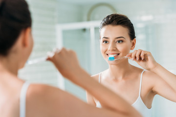 beautiful smiling girl brushing teeth at mirror in bathroom