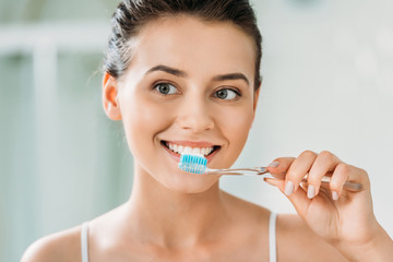 beautiful smiling girl brushing teeth in bathroom