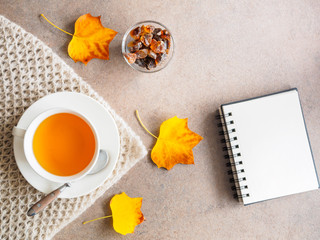 Eine Tasse Tee, Kandiszucker in einer Glasschale, Herbstblätter und ein Notizblock