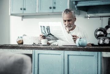 Do not disturb me. Concentrated bearded man reading news while eating tasty food