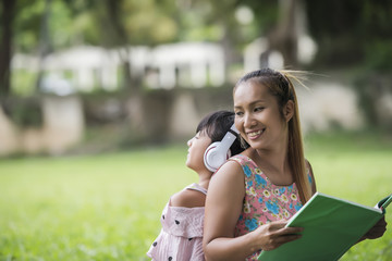 Mother and daughter reading a fairytale to her daughter listen sound with headphone in the park