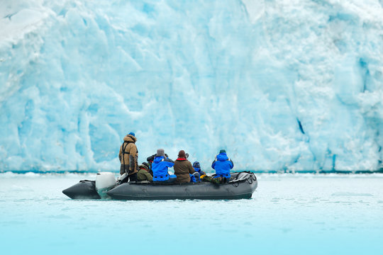 Fototapeta Nature lovers in Arctic Svalbard, Norway. Motor boat with tourists on the ice sea with glacier. Arctic cruise in winter, black powerboat with photographers, snowy icebreaker in background.