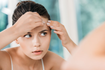 Naklejka premium selective focus of girl checking skin on forehead and looking at mirror in bathroom