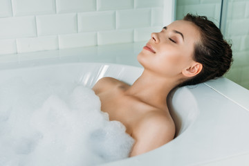 Obraz premium beautiful young woman with closed eyes relaxing in bathtub with foam