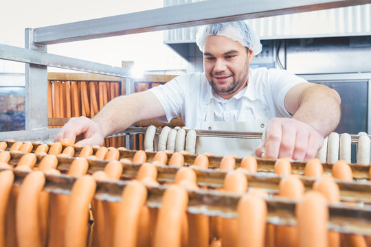 Butcher man making sausages ready to be smoked putting them on rack