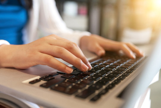 Crop shot of teenage girl typing on keyboard of laptop working on homework in library of school