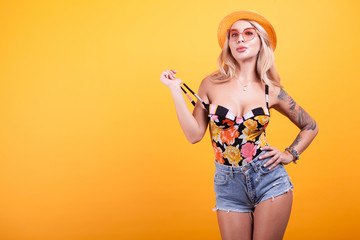 Beautiful tan Woman in swimsuit blonde haired with sunglasses in studio over yellow background