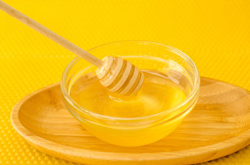 A spoon for honey in a plate with honey on a yellow background