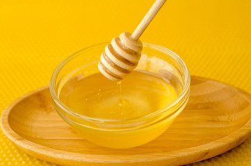 A spoon for honey in a plate with honey on a yellow background