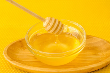 A spoon for honey in a plate with honey on a yellow background
