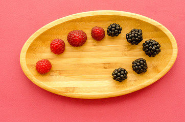 wooden plate with berries on a pink background